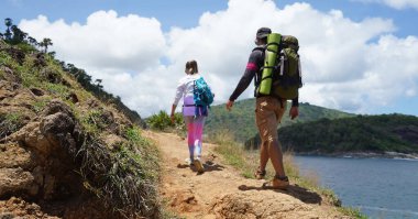 Genç bir çift okyanus manzarası sunan engebeli kayalık bir uçurumda yürüyüş yapıyor..