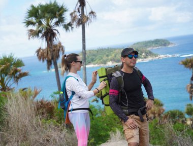 Genç bir çift okyanus manzarası sunan engebeli kayalık bir uçurumda yürüyüş yapıyor..