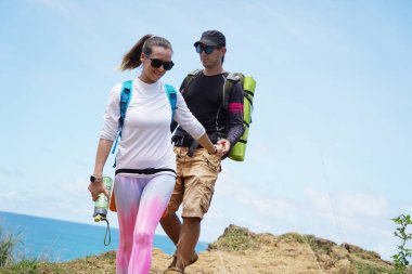 Genç bir çift okyanus manzarası sunan engebeli kayalık bir uçurumda yürüyüş yapıyor..