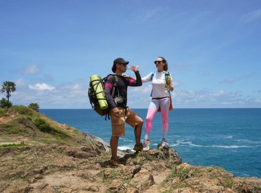 Genç bir çift okyanus manzarası sunan engebeli kayalık bir uçurumda yürüyüş yapıyor..