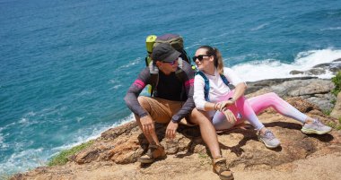 Genç bir çift okyanus manzarası sunan engebeli kayalık bir uçurumda yürüyüş yapıyor..