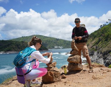 Bir erkek ve bir kadın dikkatle kayaları okyanusa yakın sanatsal bir şekilde istifliyorlar.
