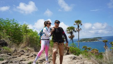 Genç bir çift okyanus manzarası sunan engebeli kayalık bir uçurumda yürüyüş yapıyor..