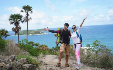 Genç bir çift okyanus manzarası sunan engebeli kayalık bir uçurumda yürüyüş yapıyor..