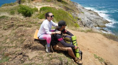 Genç bir çift okyanus manzarası sunan engebeli kayalık bir uçurumda yürüyüş yapıyor..