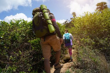 Genç bir çift okyanus manzarası sunan engebeli kayalık bir uçurumda yürüyüş yapıyor..