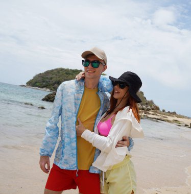 Genç bir çift kumsalda boş boş yürüyor, el ele tutuşuyor ve sıcak güneşin tadını çıkarıyor..