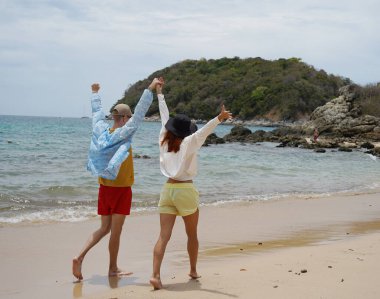 Genç bir çift kumsalda boş boş yürüyor, el ele tutuşuyor ve sıcak güneşin tadını çıkarıyor..