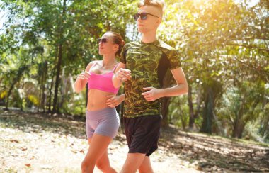 Bir adam ve bir kadın güzel bir parkta birlikte koşuyorlar, temiz havanın tadını çıkarıyorlar.