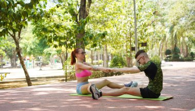 Renkli bir yoga minderinde bacaklarını açarken bir erkek bir kadına yardım ediyor..