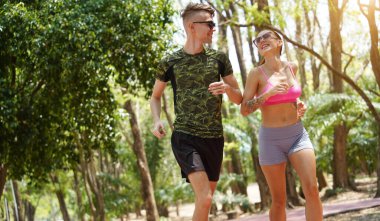 Bir adam ve bir kadın güzel bir parkta birlikte koşuyorlar, temiz havanın tadını çıkarıyorlar.