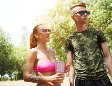 Bir adam ve bir kadın parkta birlikte koştuktan sonra şişelerden ferahlatıcı su içiyorlar..