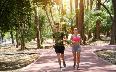 Bir adam ve bir kadın güzel bir parkta birlikte koşuyorlar, temiz havanın tadını çıkarıyorlar.
