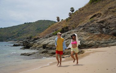 Genç bir çift kumsalda boş boş yürüyor, el ele tutuşuyor ve sıcak güneşin tadını çıkarıyor..