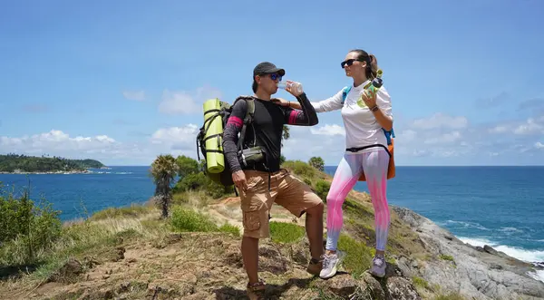 Genç bir çift okyanus manzarası sunan engebeli kayalık bir uçurumda yürüyüş yapıyor..