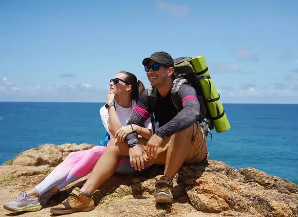 Genç bir çift okyanus manzarası sunan engebeli kayalık bir uçurumda yürüyüş yapıyor..