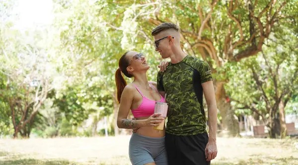 Bir adam ve bir kadın parkta birlikte koştuktan sonra şişelerden ferahlatıcı su içiyorlar..