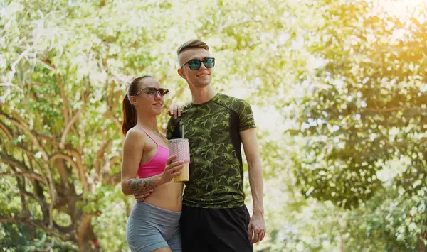 Bir adam ve bir kadın parkta birlikte koştuktan sonra şişelerden ferahlatıcı su içiyorlar..