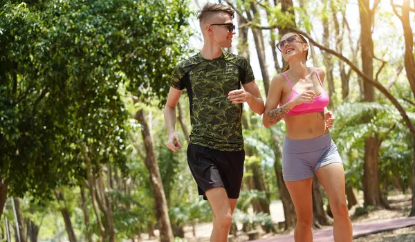 Bir adam ve bir kadın güzel bir parkta birlikte koşuyorlar, temiz havanın tadını çıkarıyorlar.