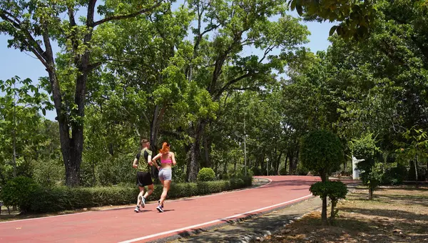 Bir adam ve bir kadın güzel bir parkta birlikte koşuyorlar, temiz havanın tadını çıkarıyorlar.