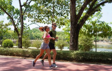 Bir adam ve bir kadın güzel bir parkta birlikte koşuyorlar, temiz havanın tadını çıkarıyorlar.