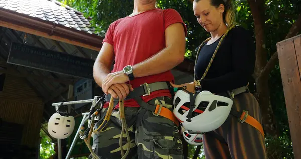 Bir erkek, halatla kaymadan önce bir kadına güvenlik amacıyla yardım ediyor..