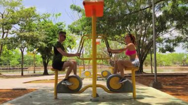 Bir adam ve kadın parkta bir makinede birlikte egzersiz yapıyorlar..