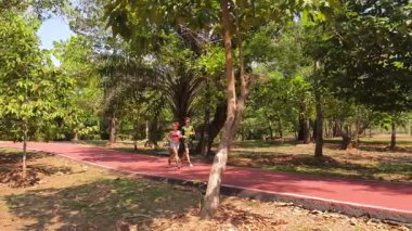 Bir adam ve bir kadın güzel bir parkta birlikte koşuyorlar, temiz havanın tadını çıkarıyorlar.