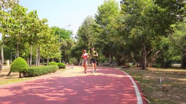 Bir adam ve bir kadın güzel bir parkta birlikte koşuyorlar, temiz havanın tadını çıkarıyorlar.