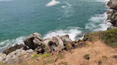 Genç bir çift okyanus manzarası sunan engebeli kayalık bir uçurumda yürüyüş yapıyor..