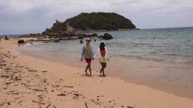 Genç bir çift kumsalda boş boş yürüyor, el ele tutuşuyor ve sıcak güneşin tadını çıkarıyor..
