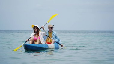 Genç çift, açık mavi bir kanoyla birlikte sarı raketlerle mutlu bir şekilde yol alıyorlar..