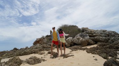 Genç bir çift kumsalda boş boş yürüyor, el ele tutuşuyor ve sıcak güneşin tadını çıkarıyor..