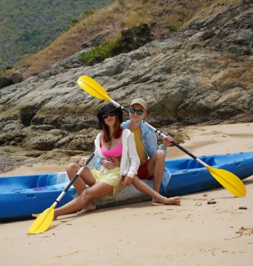 Kumsalda genç bir çift ellerinde kano kürekleri ve suda eğlenceli bir yolculuğa hazırlar..
