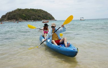 Genç çift, açık mavi bir kanoyla birlikte sarı raketlerle mutlu bir şekilde yol alıyorlar..