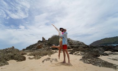 Genç bir çift kumsalda boş boş yürüyor, el ele tutuşuyor ve sıcak güneşin tadını çıkarıyor..