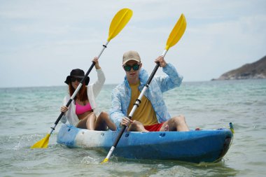 Genç çift, açık mavi bir kanoyla birlikte sarı raketlerle mutlu bir şekilde yol alıyorlar..