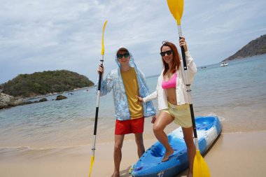 Kumsalda genç bir çift ellerinde kano kürekleri ve suda eğlenceli bir yolculuğa hazırlar..