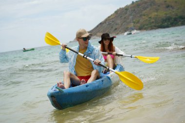 Genç çift, açık mavi bir kanoyla birlikte sarı raketlerle mutlu bir şekilde yol alıyorlar..