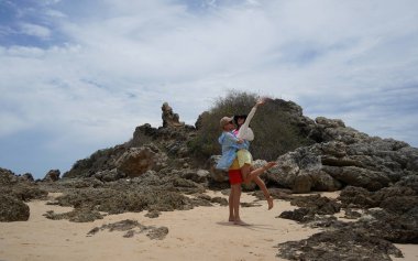 Genç bir çift kumsalda boş boş yürüyor, el ele tutuşuyor ve sıcak güneşin tadını çıkarıyor..