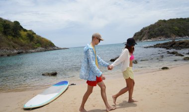 Genç bir çift kumsalda boş boş yürüyor, el ele tutuşuyor ve sıcak güneşin tadını çıkarıyor..