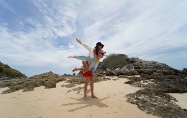 Genç bir çift kumsalda boş boş yürüyor, el ele tutuşuyor ve sıcak güneşin tadını çıkarıyor..