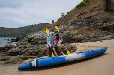 Kumsalda genç bir çift ellerinde kano kürekleri ve suda eğlenceli bir yolculuğa hazırlar..