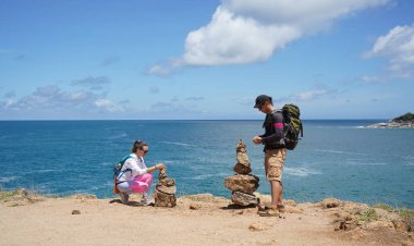 Bir erkek ve bir kadın dikkatle kayaları okyanusa yakın sanatsal bir şekilde istifliyorlar.