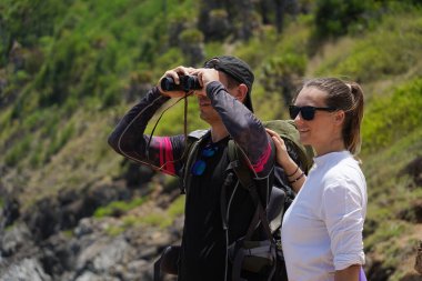 Bir erkek ve bir kadın dikkatle dürbünle uzaktan ilginç bir şeye bakıyorlar..