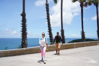 Bir erkek ve bir kadın, doğa güzelliği ve sükunetle çevrili bir yolda rahatça yürüyorlar..