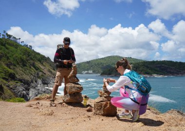 Bir erkek ve bir kadın dikkatle kayaları okyanusa yakın sanatsal bir şekilde istifliyorlar.