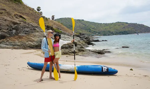 Kumsalda genç bir çift ellerinde kano kürekleri ve suda eğlenceli bir yolculuğa hazırlar..