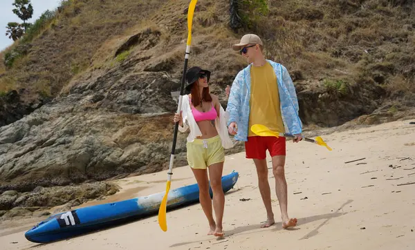 Kumsalda genç bir çift ellerinde kano kürekleri ve suda eğlenceli bir yolculuğa hazırlar..