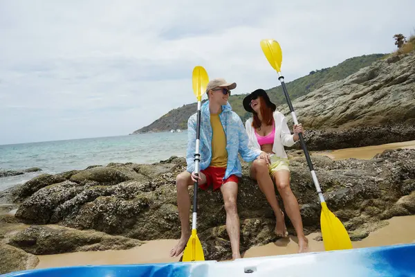 Kumsalda genç bir çift ellerinde kano kürekleri ve suda eğlenceli bir yolculuğa hazırlar..